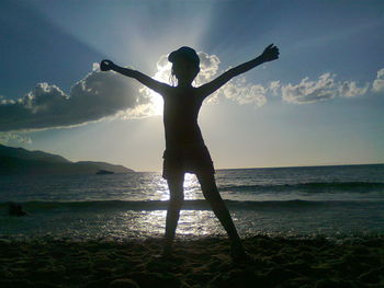 Silhouette girl with arms outstretched while standing on sea shore