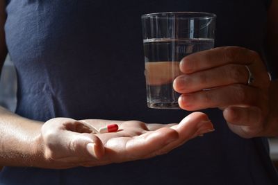 Midsection of woman holding capsule and drinking glass