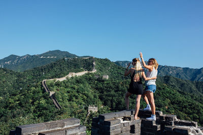 Young couple standing on rock against clear blue sky