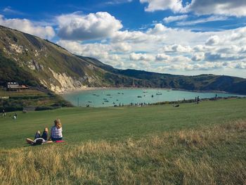 Woman sitting on field by lake against sky