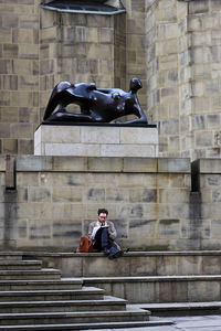 Statue of man sitting against building