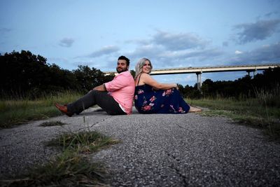 Young couple sitting on grass against sky