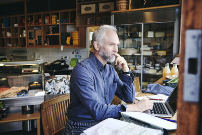 Thoughtful salesman using laptop at table in deli