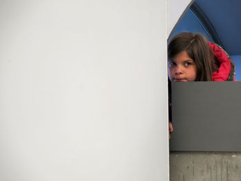Portrait of girl hiding against wall