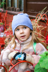 A young woman in a blue hat admires a vibrant red flower in a garden filled with colorful blooms. 