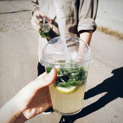 Cropped hand holding drink glass by friend on street