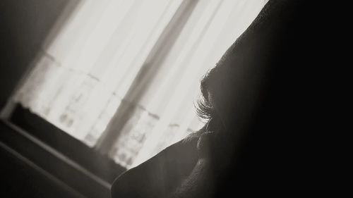 Close-up of woman looking through window at home