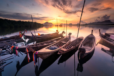 Sailboats moored in lake against sky during sunset