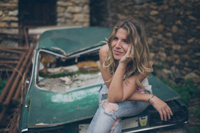 Young woman looking away while sitting on abandoned car
