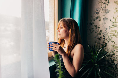 Young woman drinking coffee in window