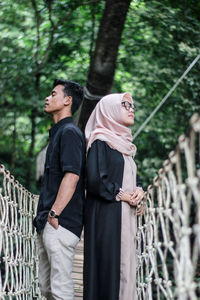 Couple standing back to back on footbridge in forest