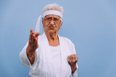 Portrait of senior woman doing karate against blue background