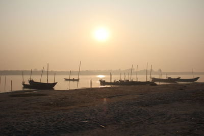 Sailboats moored in sea at sunset