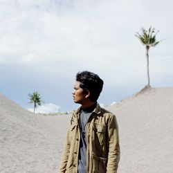 Young man standing on sand at beach against sky