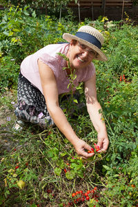 Portrait of smiling woman harvesting cherry tomatoes on field