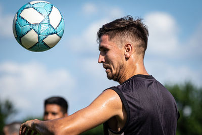 Young man and woman ball on soccer field against sky