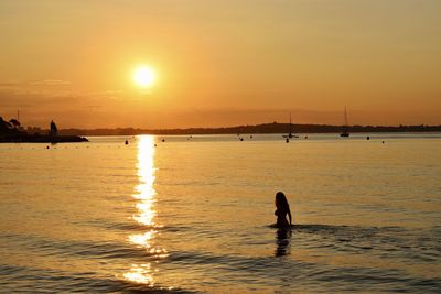 Silhouette people on sea against sky during sunset