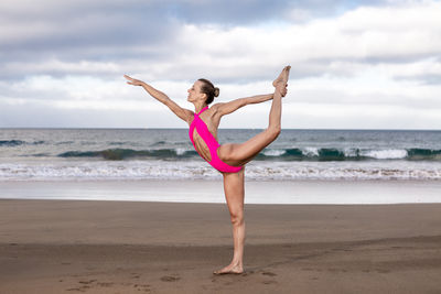 Full length of young woman exercising at beach against sky