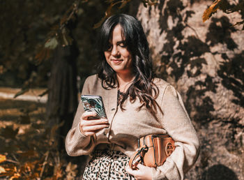 Portrait of smiling woman holding smart phone outdoors