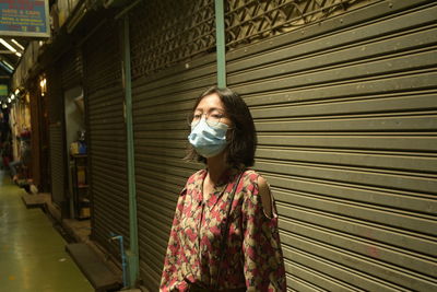 Portrait of woman wearing mask standing against closed shutter