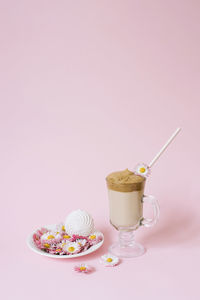 Dalgona coffee in a transparent cup with a paper tube, a plate with daisies and marshmallows. 