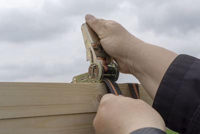 Close-up of hand holding wood against sky