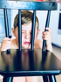 Cute boy with eyes closed crouching while holding chair 