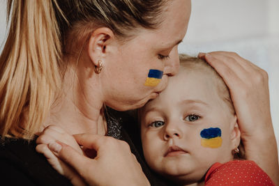 Mother kissing daughter with ukrainian flag paint on face