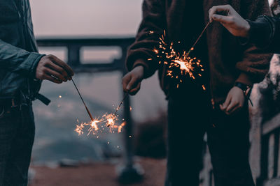 Midsection of people holding sparklers at night