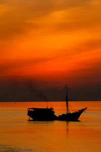 Silhouette ship in sea against orange sky