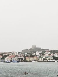 Buildings by sea against clear sky