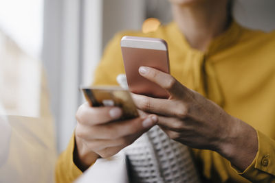 Blond businesswoman sitting at window, doing a paymant with smartphone and creditcard