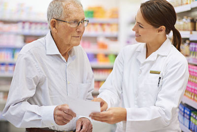 Pharmacist helping with prescription to senior man at pharmacy store