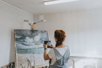 Artist taking picture of painting in studio