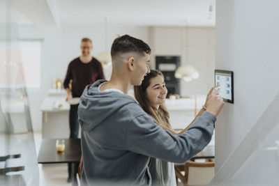 Brother and sister using digital tablet mounted on wall at smart home