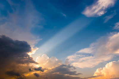 Low angle view of sunlight streaming through clouds