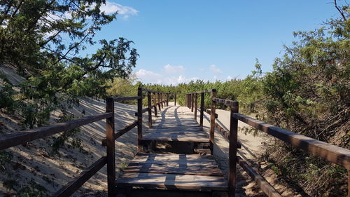 Footbridge amidst trees against sky