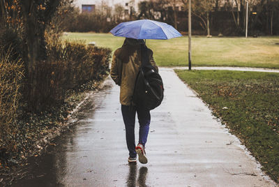 Woman with umbrella walking on wet footpath