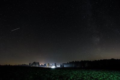 Scenic view of starry sky over trees growing on field