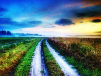 Road amidst field against sky during sunset