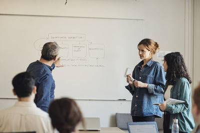 Male teacher explaining diagram to students while pointing at whiteboard in classroom