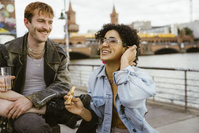 Smiling non-binary person adjusting sunglasses while having pizza with friends in city