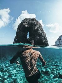 Rear view of woman on rock by sea against sky