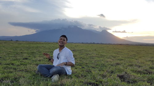 Full length of man sitting on field against sky