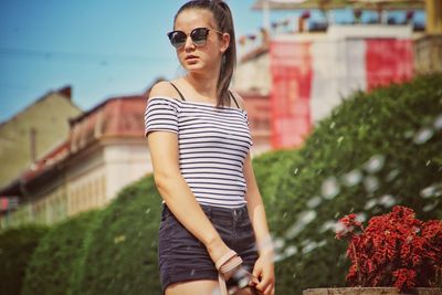 Water spraying against woman wearing sunglasses against buildings