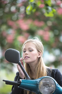 Young woman touching lips looking in side-view mirror of motor scooter