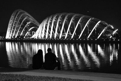 Rear view of people standing by illuminated bridge against sky at night