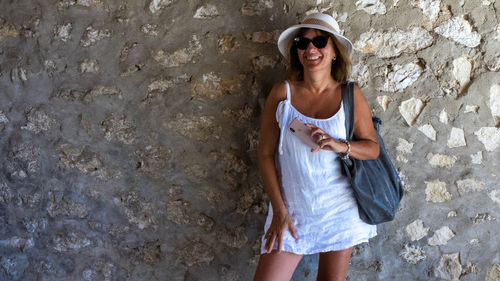 Young woman wearing sunglasses standing against wall