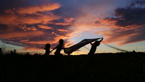 Silhouette men standing on field against sky during sunset