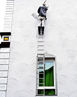 Low angle view of worker on ladder against building